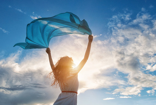 Vrouw met sjaal in de wind onder zonnige bewolkte hemel